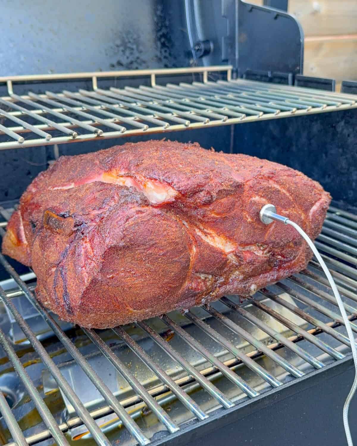 A seasoned pork shoulder on the smoker with a temperature probe attached.