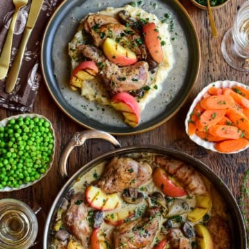 Succulent rabbit braised with apples and vegetables, presented on a rustic plate with herbs, alongside sides of greens and carrot slices.