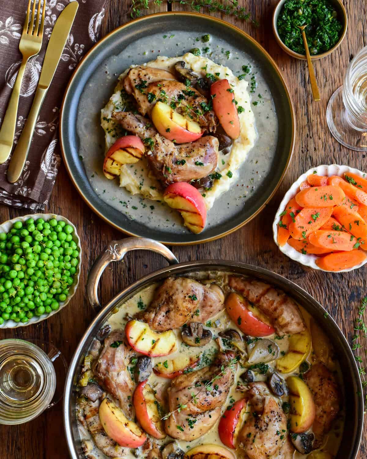 Succulent rabbit braised with apples and vegetables, presented on a rustic plate with herbs, alongside sides of greens and carrot slices.