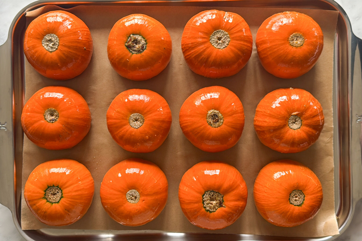 Twelve pumpkins upside down on a tray ready to be baked.