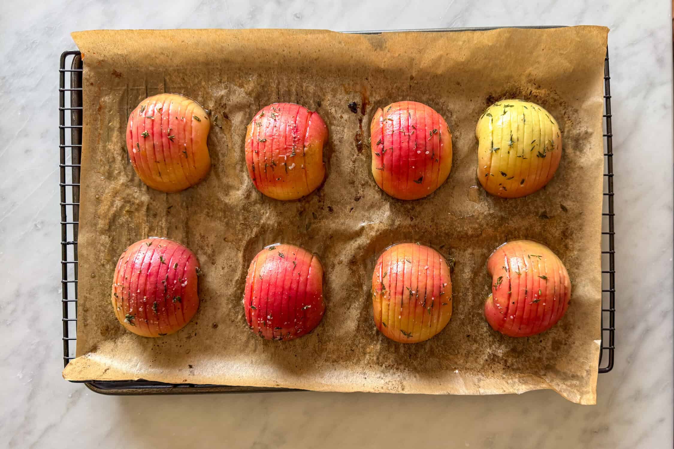 Eight baked Hasselback apples on a parchment-lined rack to cool.
