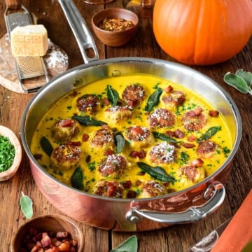 Turkey meatballs cooked in a pumpkin-sage sauce in a copper skillet, garnished with sage leaves and grated cheese, with pumpkins and spices in the background.