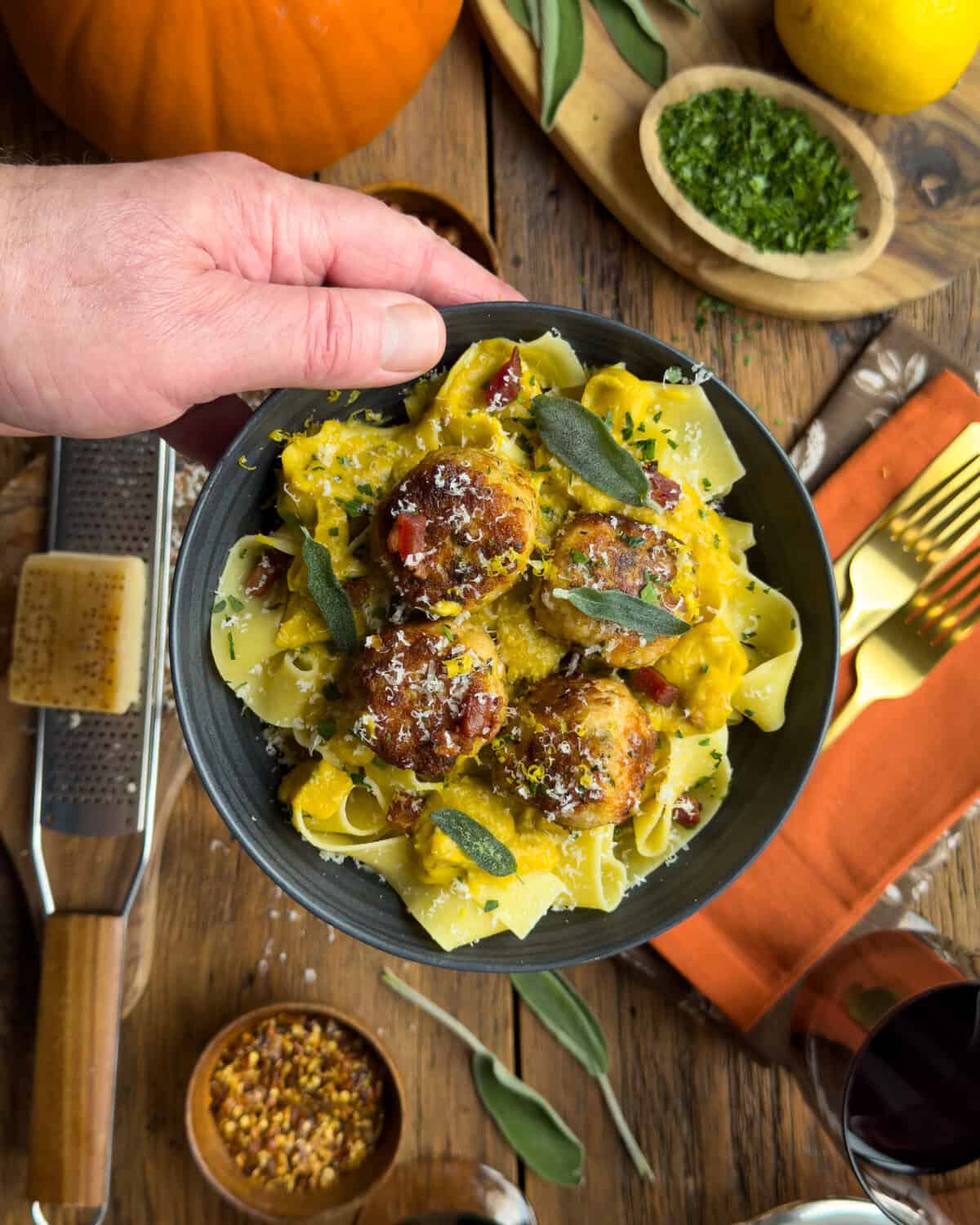 Close-up of turkey meatballs served with pumpkin sage sauce and pasta, garnished with fresh sage leaves, on a rustic wooden table.