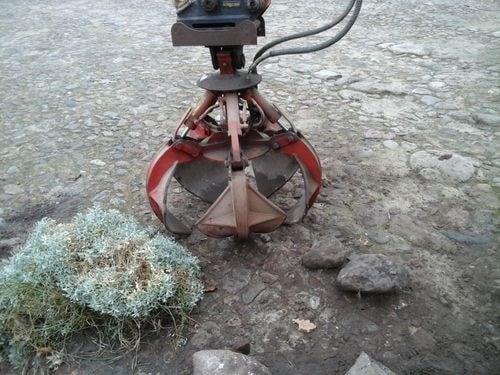 Jordbearbejdningsmaskine i naturen med sten og planter i baggrunden.
