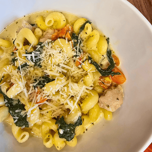 Delicious creamy garlic and herb tomato spinach pasta served in a white bowl, perfect for a comforti.