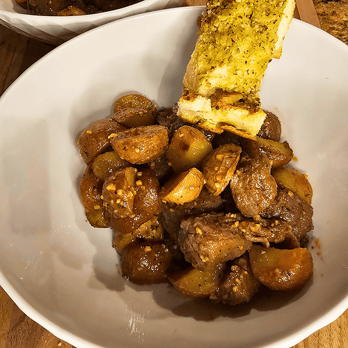 Juicy garlic butter steak with roasted potatoes in a white bowl.
