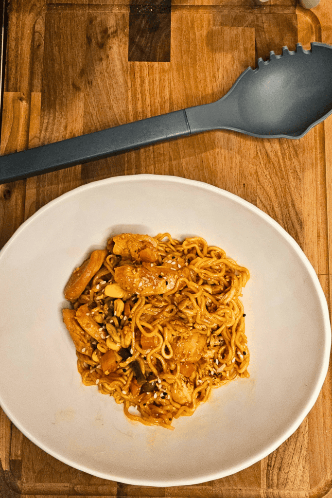 Delicious chicken noodle stir-fry with vegetables on a white plate.