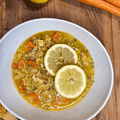 Healthy chicken soup with lemon slices, carrots, and rice in a white bowl.