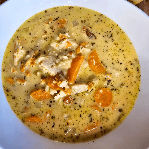 Comforting creamy chicken and rice soup with vegetables in a white bowl.
