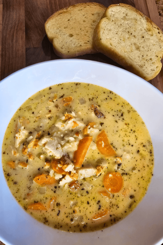 Comforting creamy chicken and rice soup with vegetables in a white bowl.