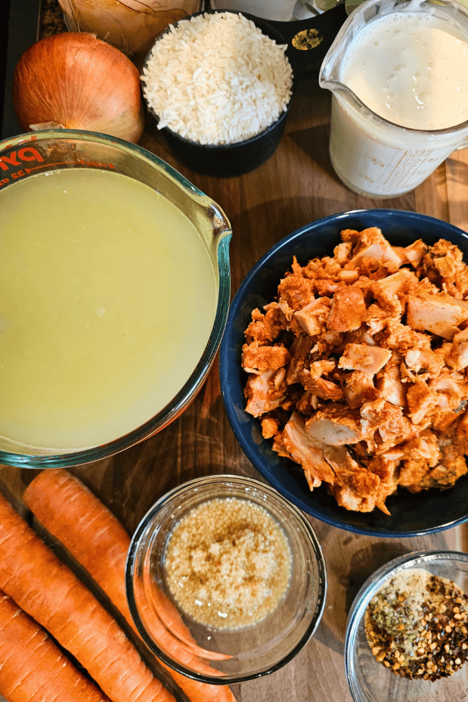 Fresh ingredients for creamy chicken and rice soup including chicken, rice, carrots, onion, and cream.