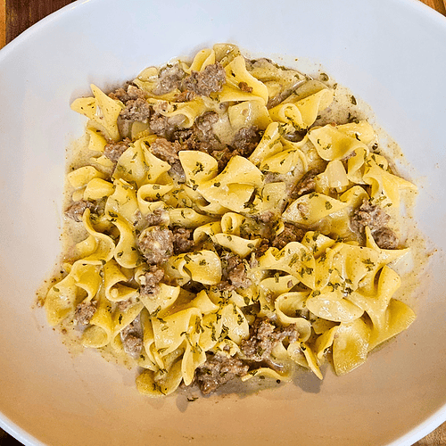 Creamy beef stroganoff with pasta in a white bowl on wooden table.