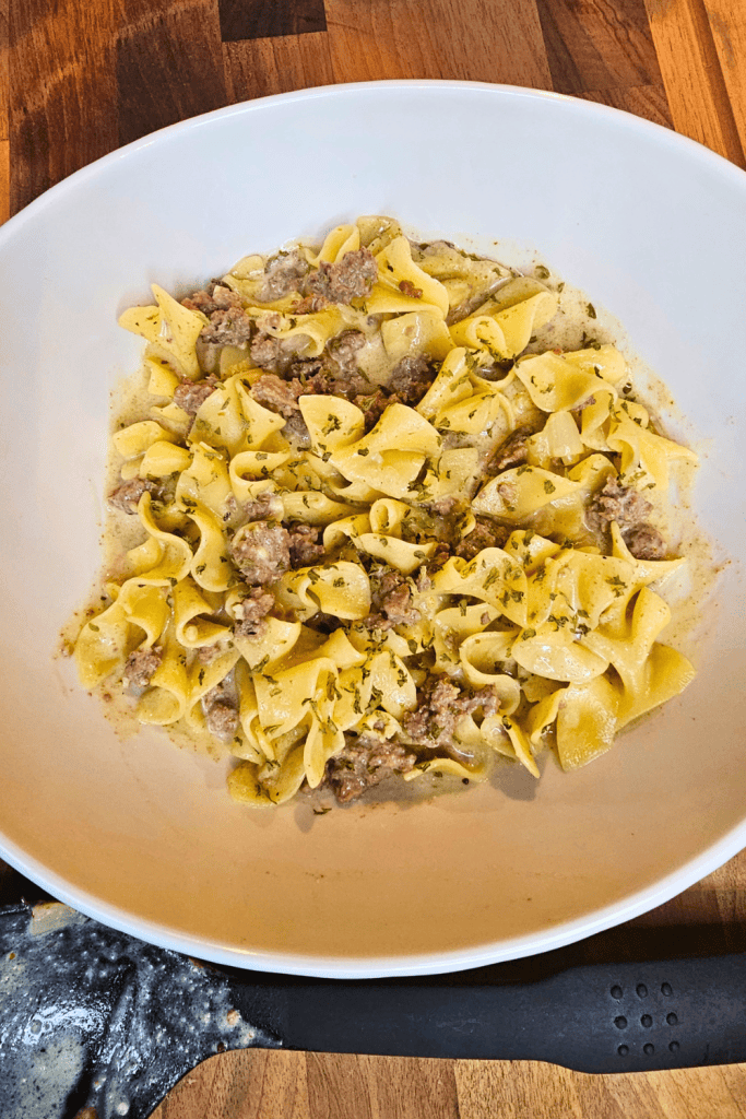 Creamy beef stroganoff with pasta in a white bowl on wooden table.