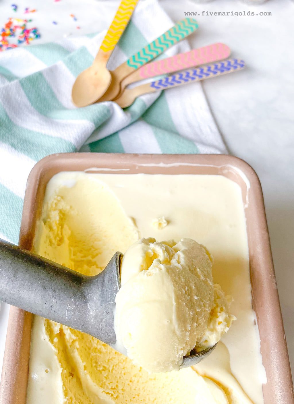 Ice cream scoop filled with marshmallow vanilla ice cream sitting on top of a loaf pan containing ice cream