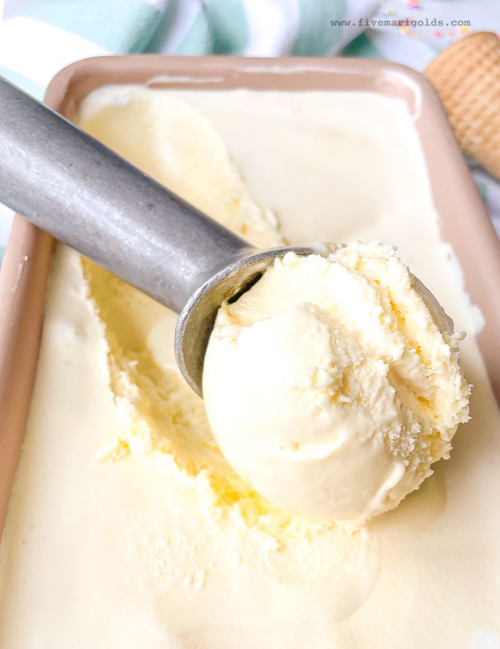 Ice cream scoop filled with marshmallow vanilla ice cream sitting on top of a loaf pan containing ice cream