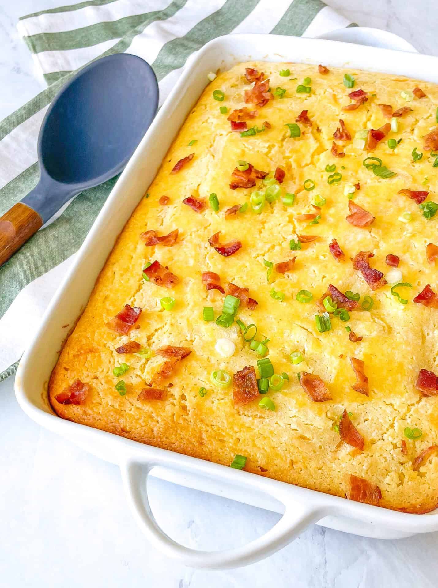 Casserole dish containing cornbread casserole with bacon and green onions on top