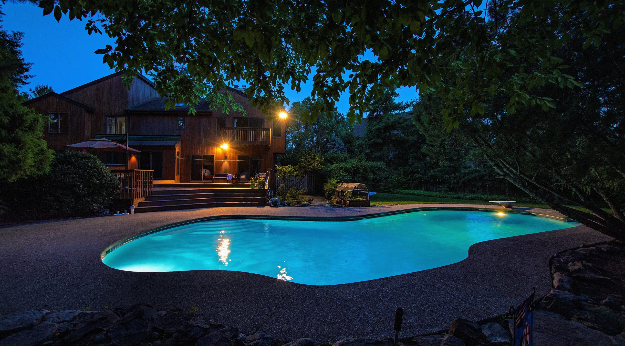 Twilight pool scene with illuminated water framed by home and deck.