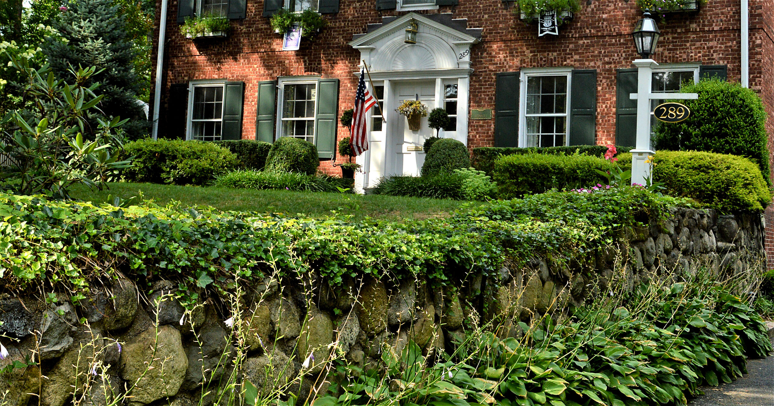 Classic brick colonial home with ivy-covered stonework in established community.