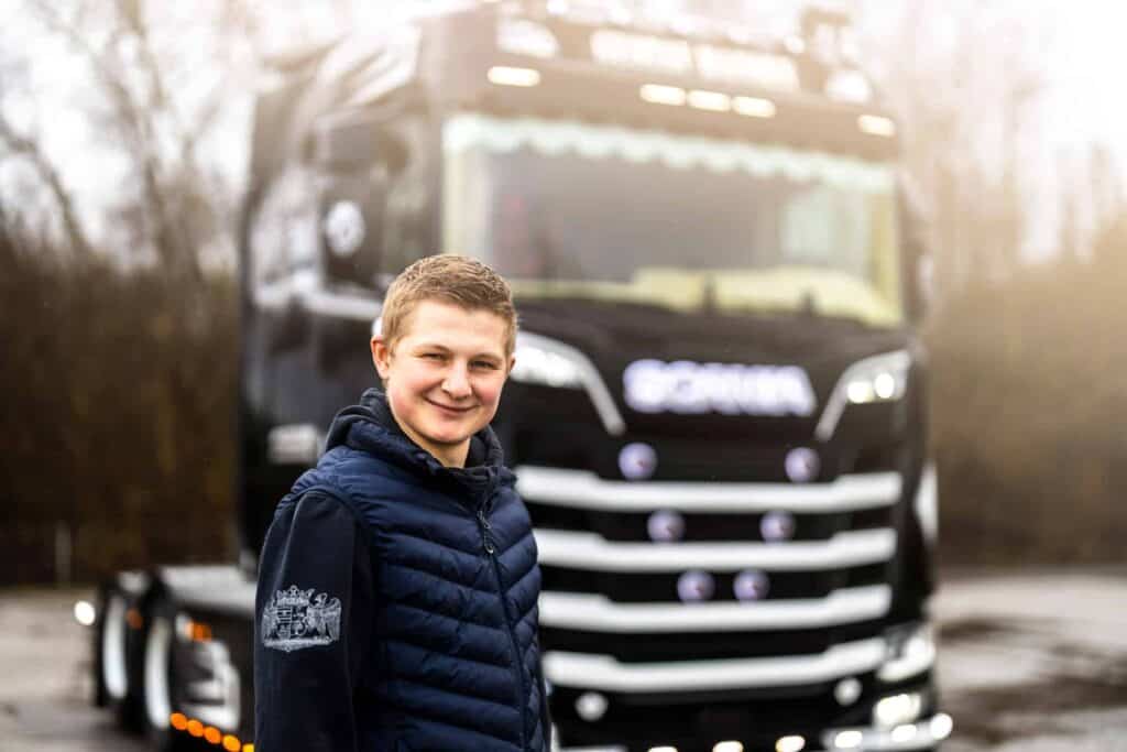 Et billede af en smilende Gustav Hansen foran en af hans sorte lastbiler.