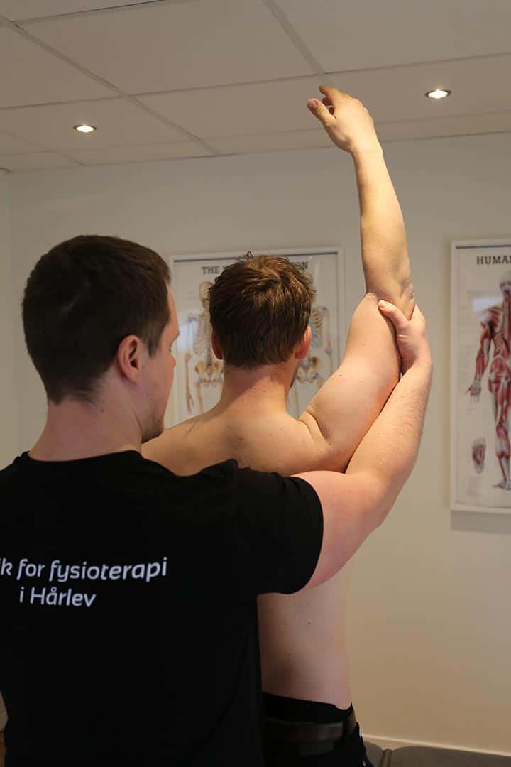 En fysioterapeut fra Klinik for fysioterapi i Hårlev undersøger bevægeligheden i en patients skulder ved at føre armen opad