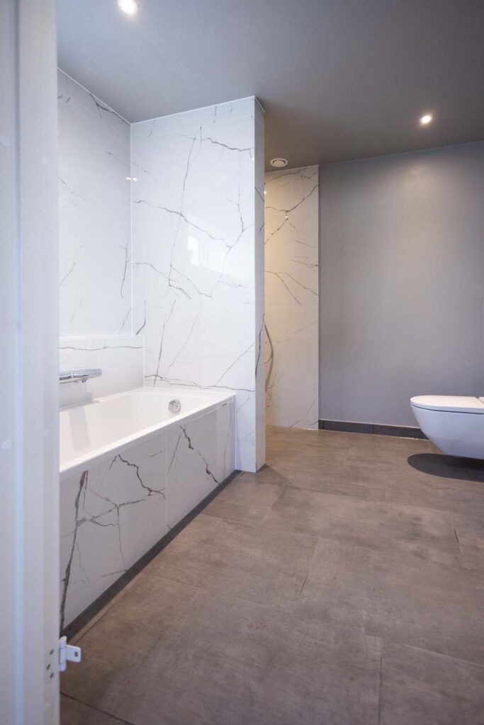 Badeværelse med hvidt badekar og væghængt toilet.