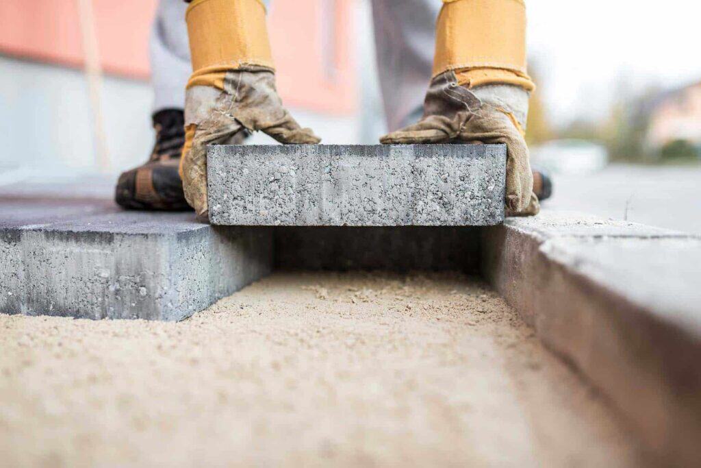Arbejder lægger betonflise på ny belægning udendørs.