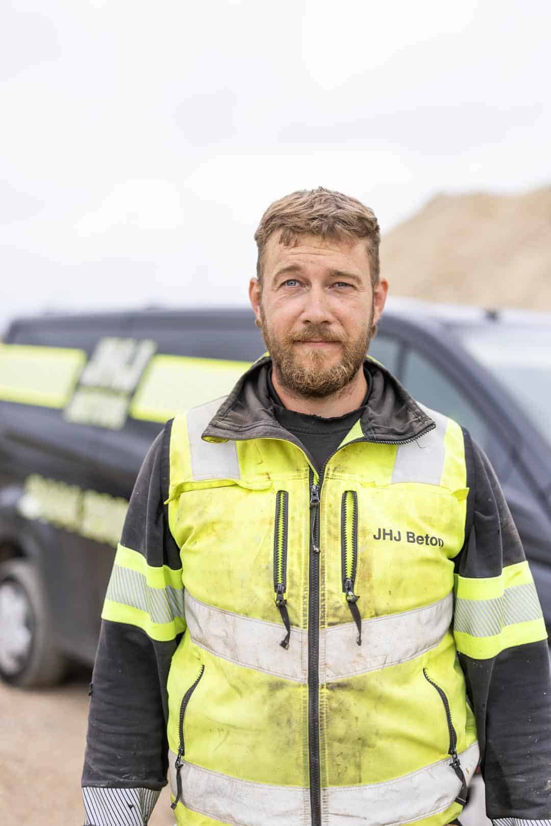 Bygningsarbejder i høj synlighedsvest foran byggepladsen, klar til arbejde.