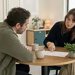 Deux personnes discutent autour d’une petite table ronde, l’une montrant des notes manuscrites sur une feuille.