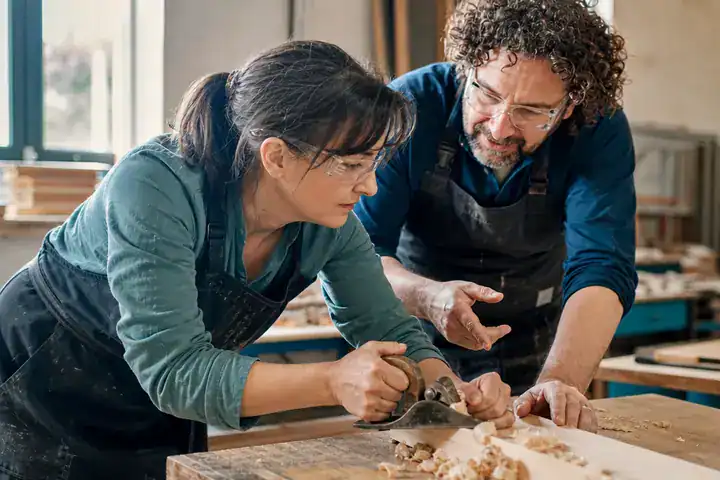 Une femme apprend la menuiserie en atelier de formation, accompagnée d’un formateur