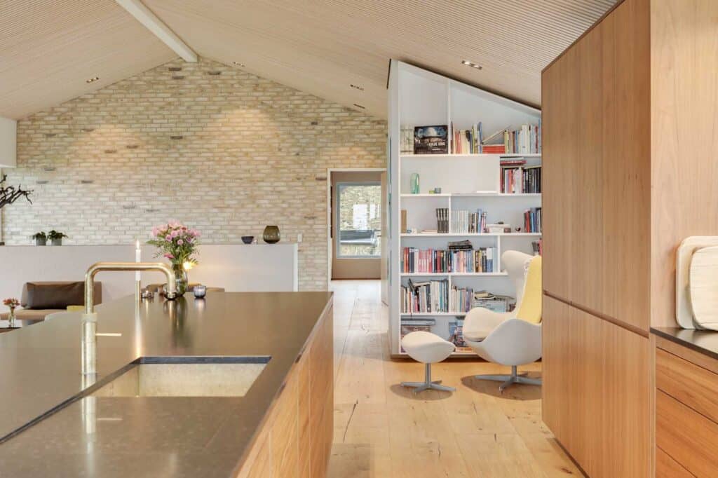 Køkken set fra stuen med indbygget reolvæg i rå mursten.