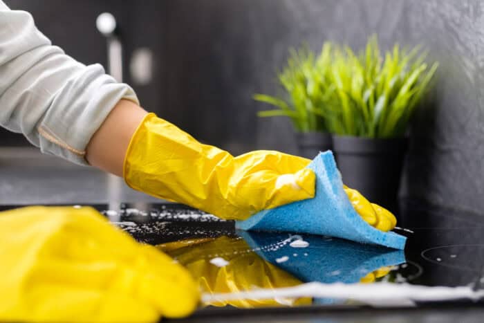 A girl washes the stove with a blue sponge in yellow gloves