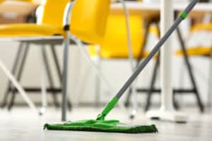 Green plastic mop cleaning laminated light dirty floor closeup