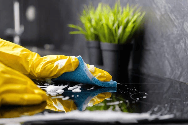 Yellow-gloved hand cleaning countertop with sponge and soap