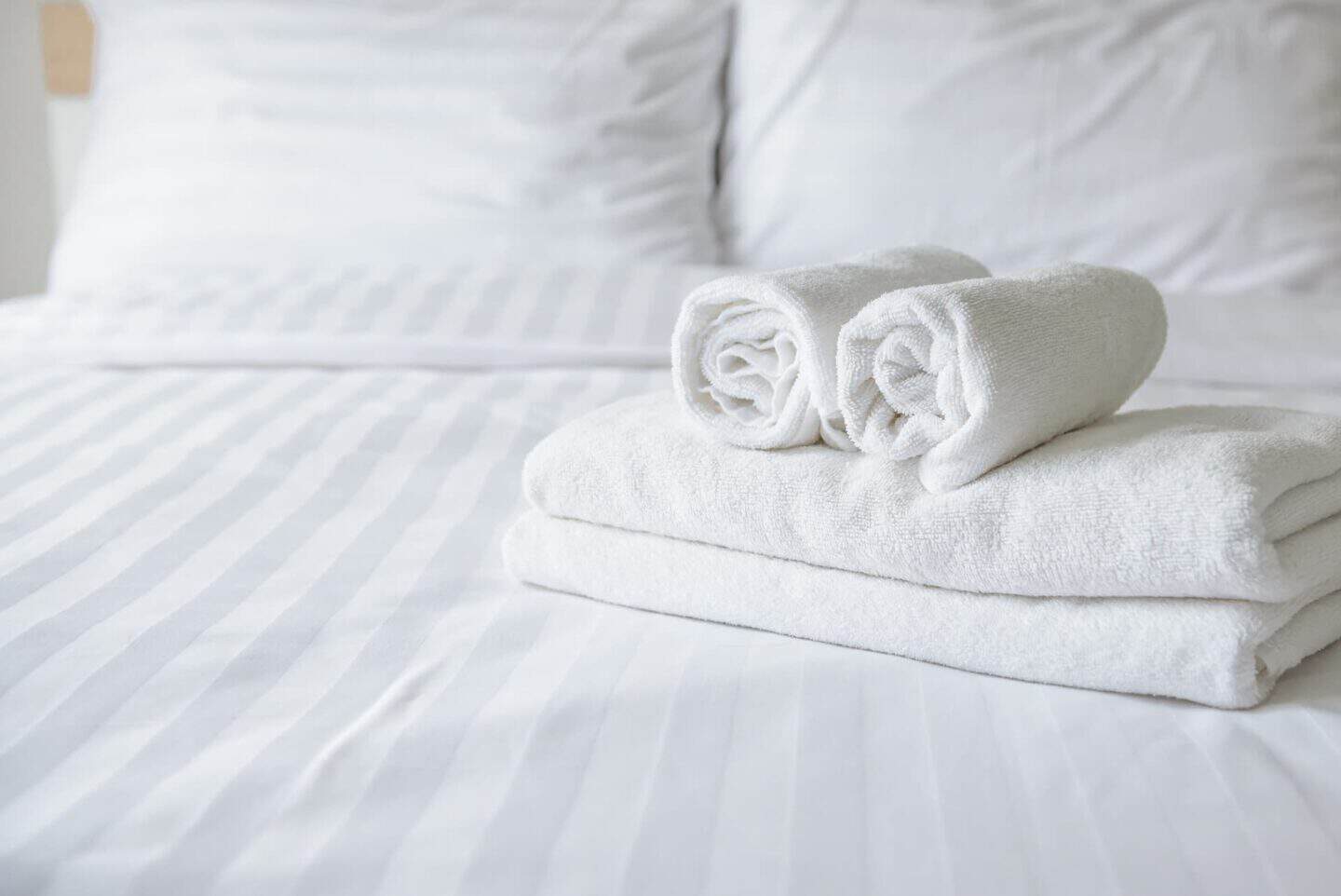 Neatly rolled white towels on hotel bed
