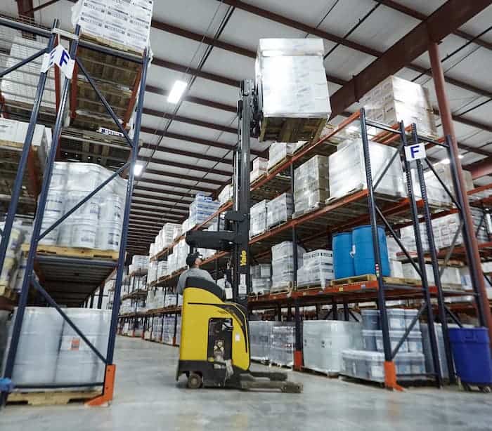 Forklift lifting pallet in large warehouse aisle