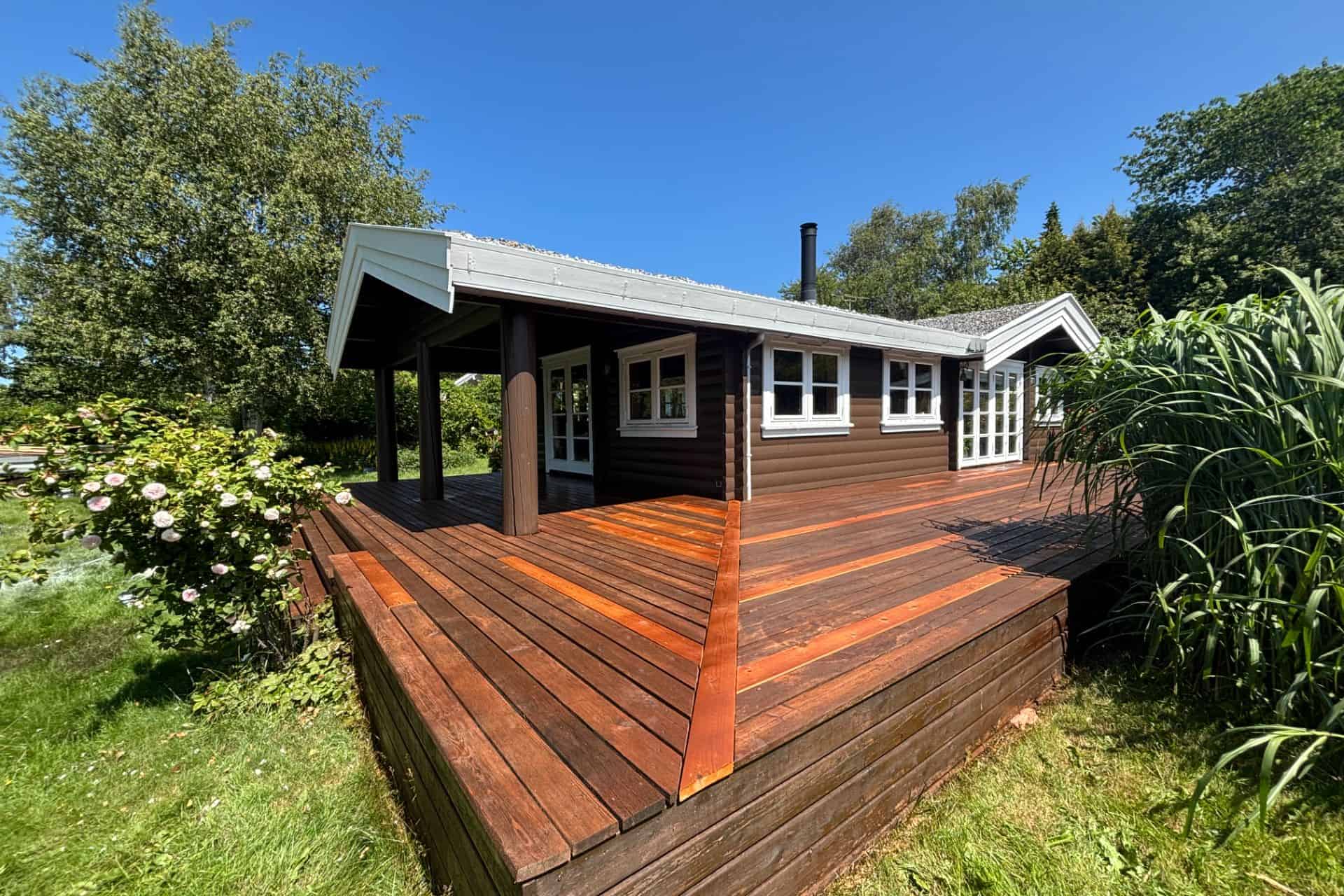 Stor træterrasse i haven foran et nymalet mørkt hus
