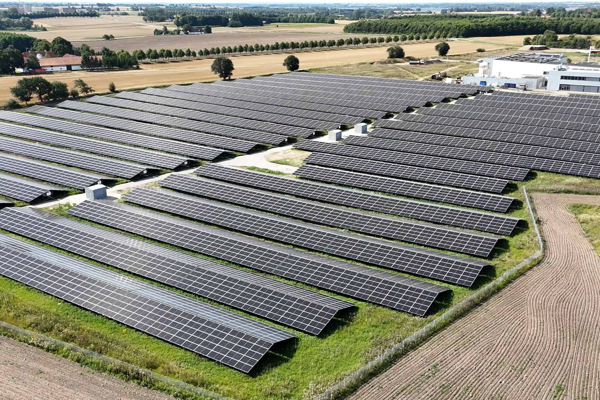 Stor solcellepark med solpaneler i landbrugsområde.