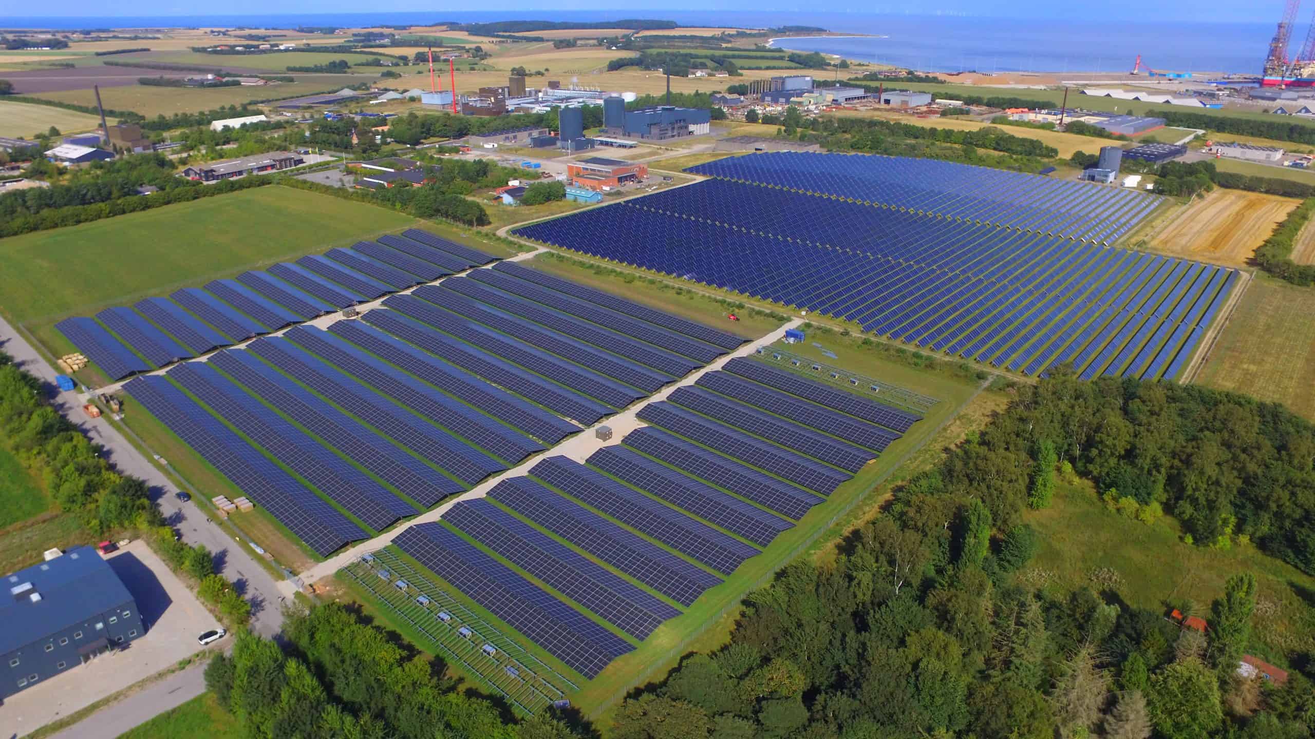 Stort solcelleanlæg med mange solpaneler i et landbrugsområde.