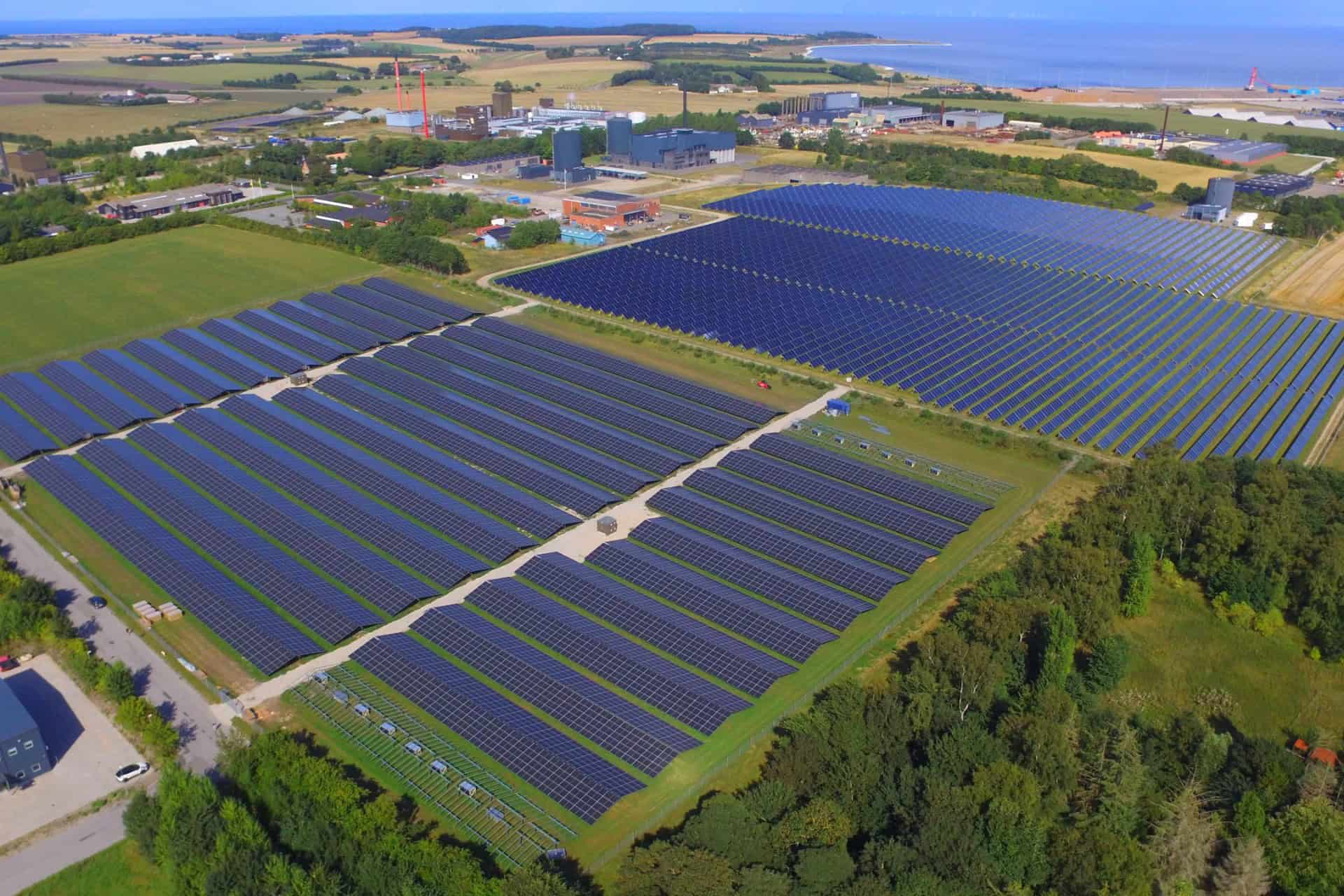 Stort solcelleanlæg i Danmark med mange solpaneler under klar himmel.