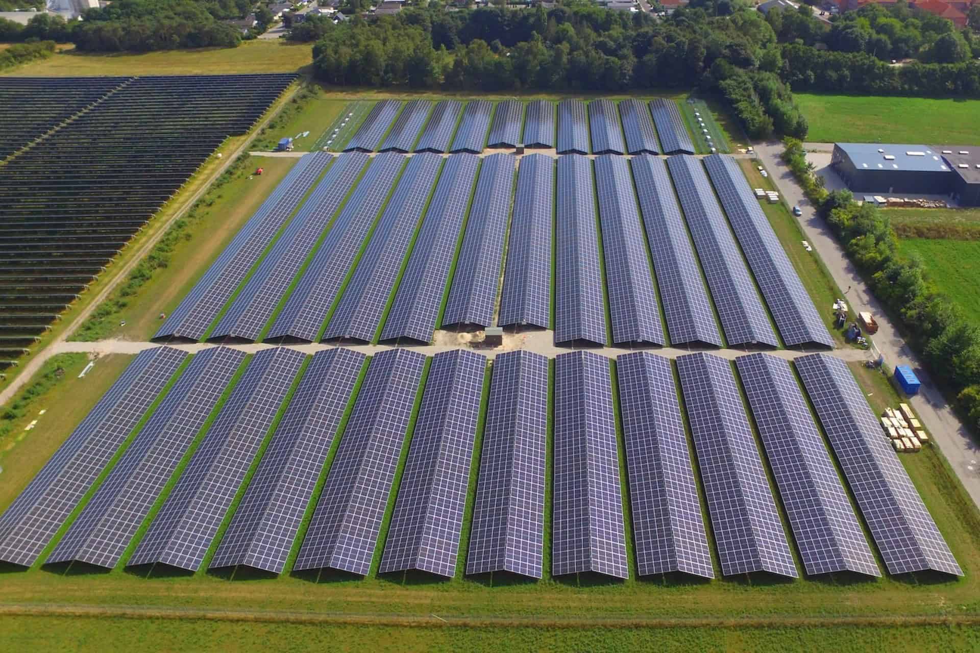 Stor solcellepark med mange solpaneler i solrigt landskab.