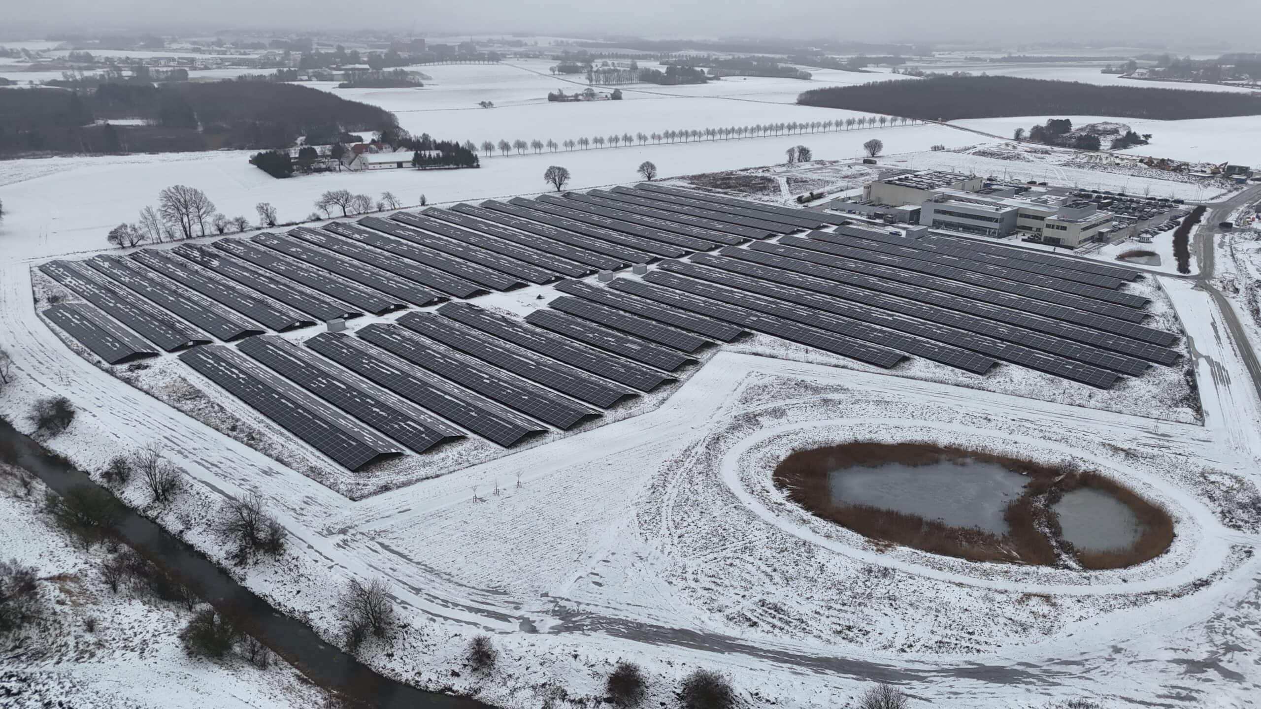 Stort solcelleanlæg dækket af sne i vinterlandskab.