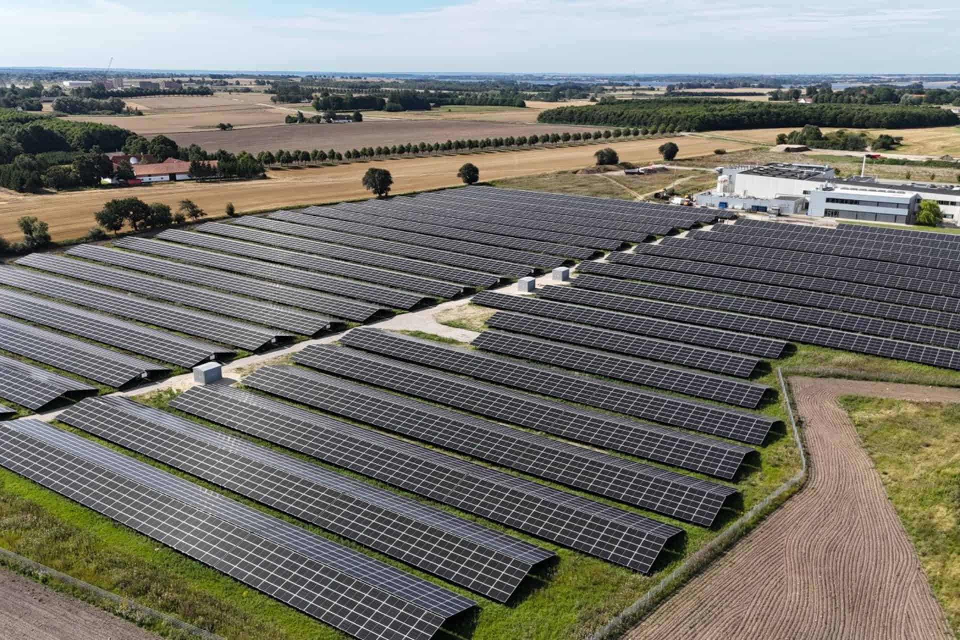 Stort solcelleanlæg med mange solpaneler i åbent landskab.