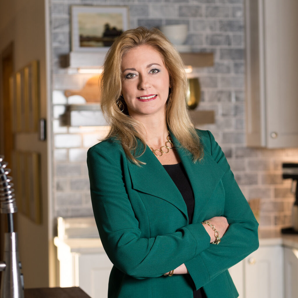 Diane Welhouse, offering business consulting services, smiles at the camera, is wearing a professional forest green blazer in a professional office setting.