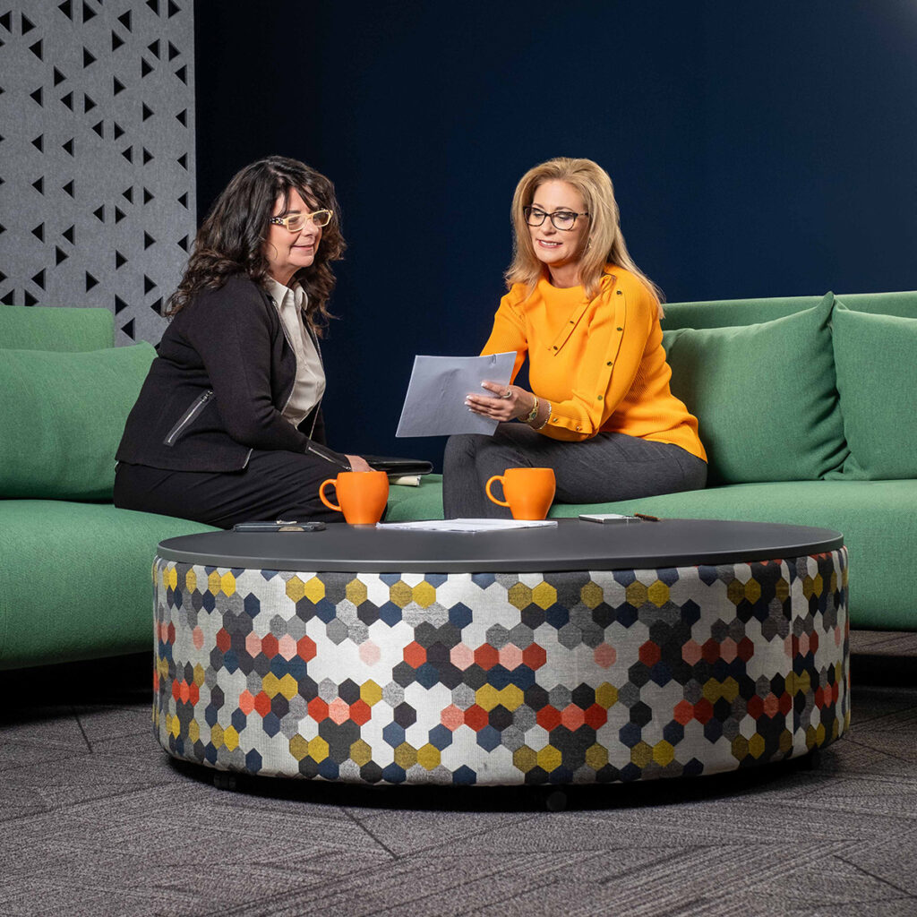 Diane Welhouse and a coaching client sit on a green couch, reviewing a document Diane is holding.