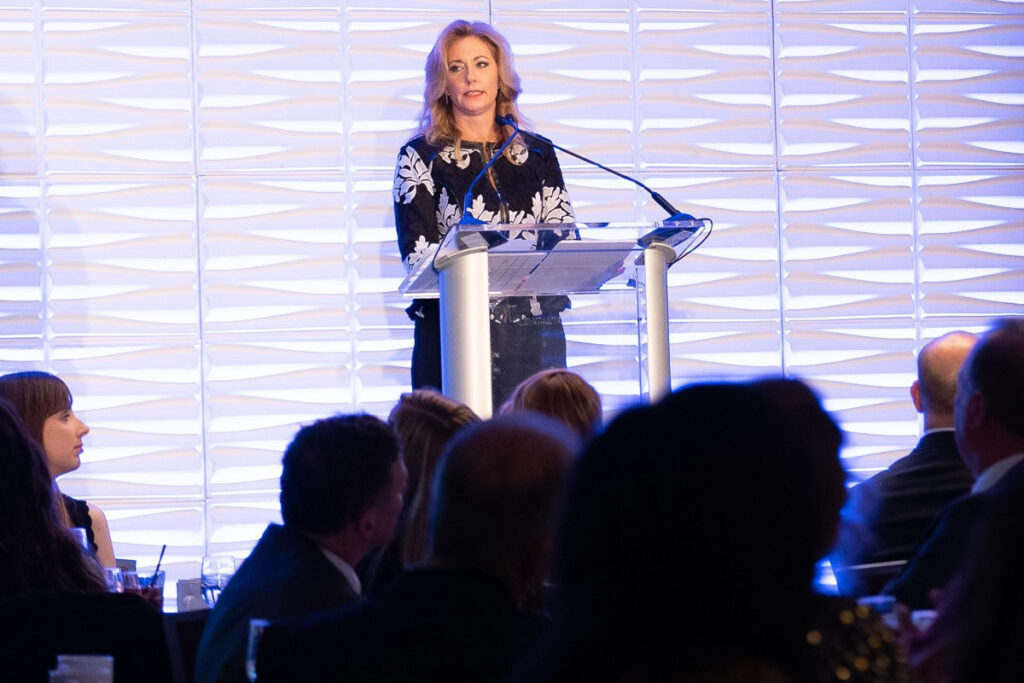 Diane Welhouse, a professional speaker, stands at a podium in front of a crowd.