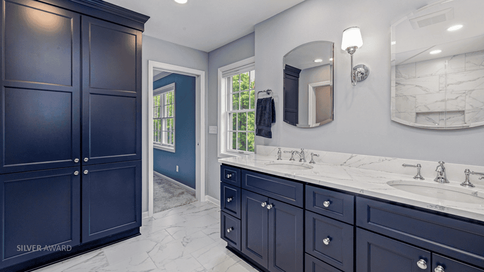 Bathroom with dual vanity and a large linen closet. Cabinetry is deep blue with white marble countertops and floors.