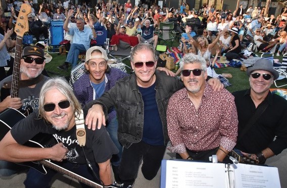Group of musicians performing at an outdoor concert in Channel Islands Harbor with audience in backg.