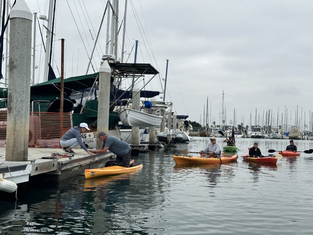People kayaking and preparing boats at Channel Islands Harbor marina in California.