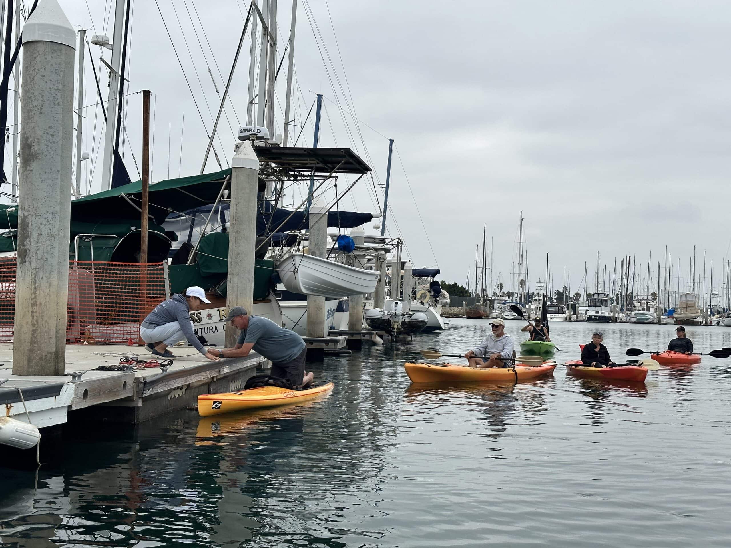 People kayaking and preparing boats at Channel Islands Harbor marina in California.