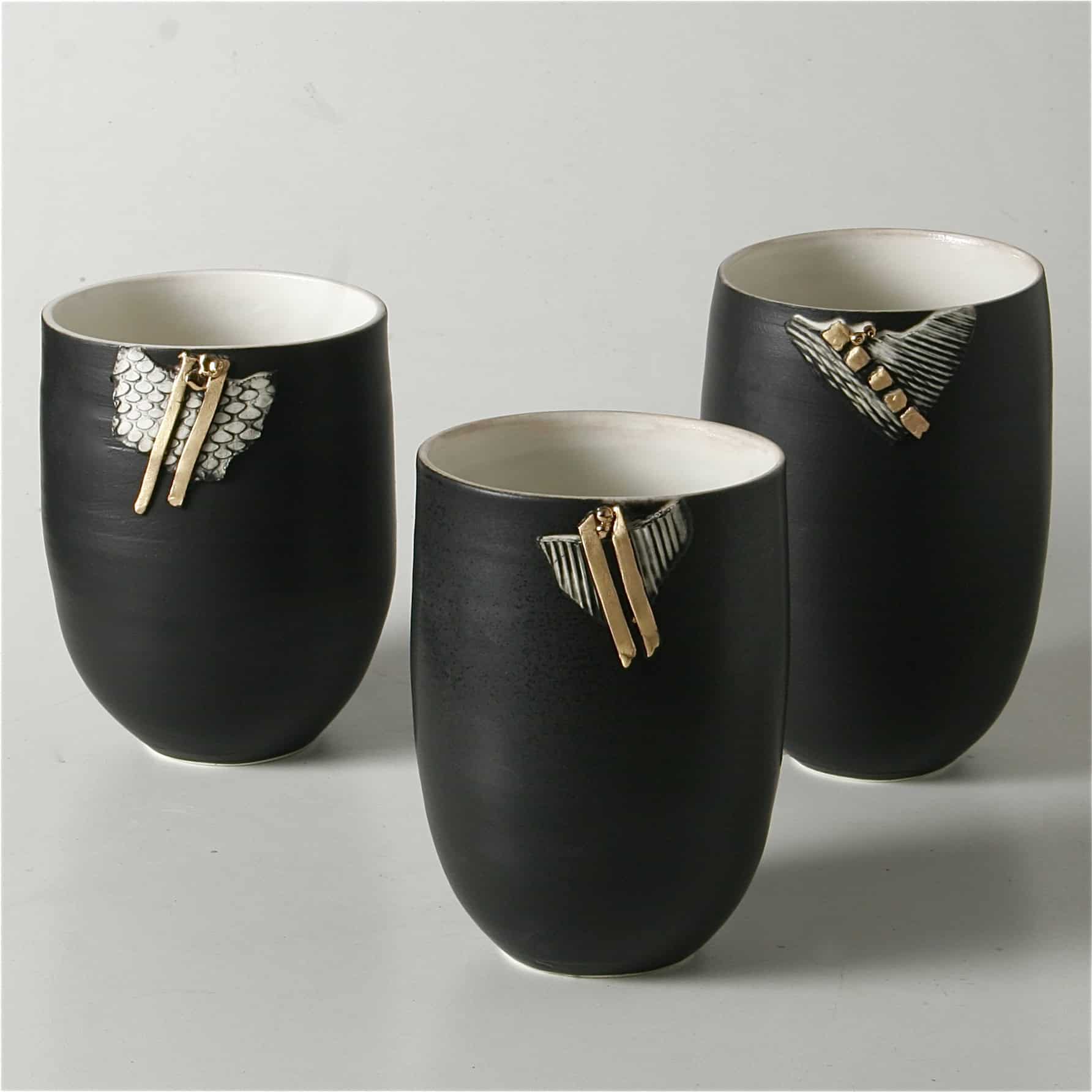 Tre sorte keramiske krus med elegante guld- og sølvdetaljer, perfekt til moderne hjem.